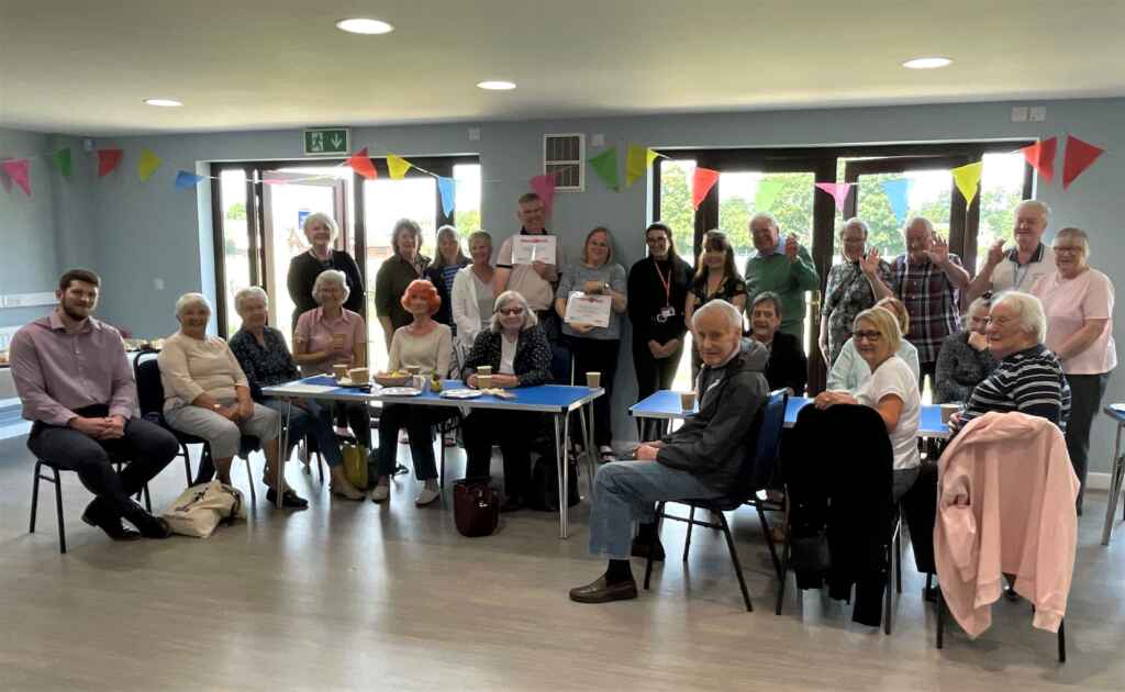 Group of people standing and sitting at tables in a community centre