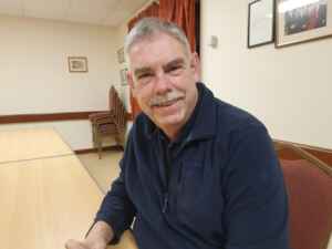 Picture of a man sat at a table facing camera smiling